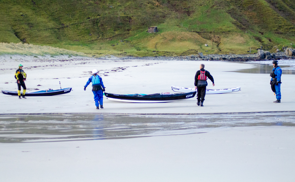 Paddlers carrying Edge kayaks across the sand towards the surf in Hoddevik
